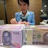 A bank teller counts baht notes in Bangkok, Thailand. (Photo: AFP/VNA)