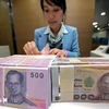 Un caissier de banque compte les billets de baht à Bangkok, en Thaïlande. (Photo : AFP/VNA)