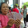 A woman holds up her share of the 10,000-baht cash handout, which is deemed part of the government's economic stimulus plan. (Photo: Bangkokpost) 