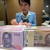 Una cajera de banco cuenta billetes de baht en Bangkok, Tailandia. (Foto: AFP/VNA) 