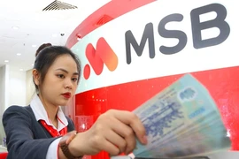 A bank teller counts money at a transaction office in Hanoi. (Photo: VNA)