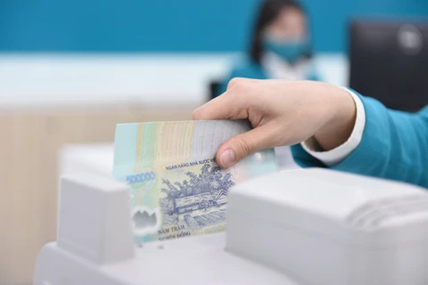 A bank teller counts money at a transaction office in Hanoi. (Photo: vietnamfinance.vn)