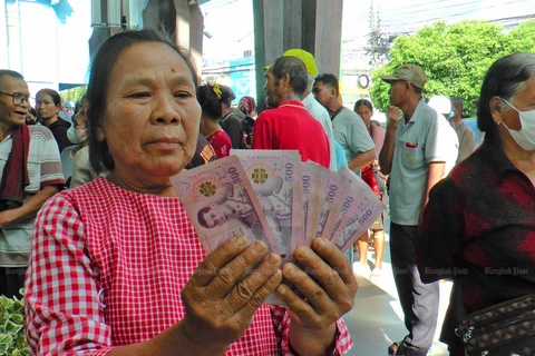 A woman holds up her share of the 10,000-baht cash handout, which is deemed part of the government's economic stimulus plan. (Photo: Bangkokpost) 