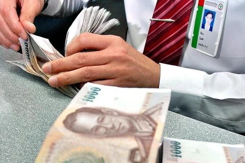 A bank employee counts baht in Bangkok, Thailand. (Photo: AFP/VNA)