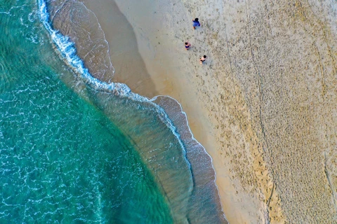 Чистое синее море брызгает белой пеной, когда волна ударяется о гладкий песчаный берег. (Фото: Чан Ле Лам/ВИА)