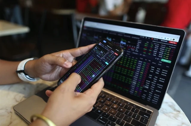 A mobile phone and laptop screen showing stock indices. The disparity in interest rate, monetary policies, volatile exchange rates and political fluctuations have significantly influenced foreign investors' actions. (Photo: VNA)