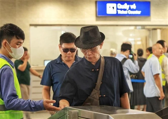 Passengers swipe their cards to board the train as instructed by staff (Photo: VNA)