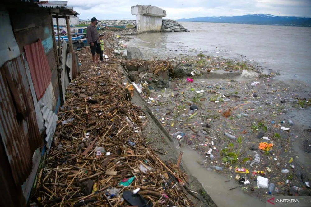 Seorang ayah dan anak menyaksikan sampah yang tersapu ke pantai dekat Teluk Palu, Sulawesi Tengah, Indonesia. (Foto: antaranews.com)