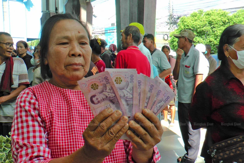 A woman holds up her share of the 10,000-baht cash handout, which is deemed part of the government's economic stimulus plan. (Photo: Bangkokpost) 