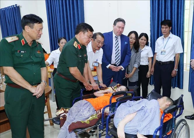 Le vice-ministre de la Défense, Hoàng Xuân Chiên, et l’ambassadeur des États-Unis au Vietnam Marc Knapper, au chevet d’une victime de l’agent orange au Centre de soins, d’éducation et de traitement des victimes de l’agent orange/dioxine de Hanoi. Photo : VNA